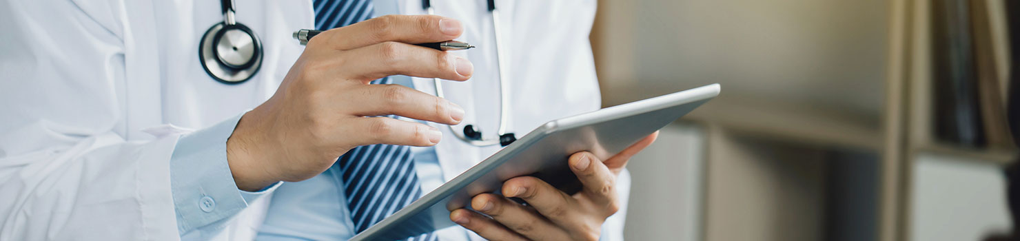 A male doctor with a white coat holding a pen and an iPad.