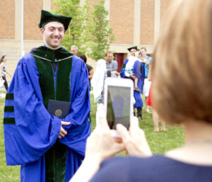 Female taking picture of male LECOM Graduate in front of Warner Theater in Erie, PA.