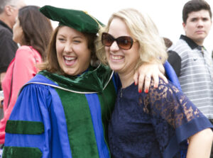 LECOM Graduate students smiling with blonde friend for photo after LECOM Erie graduation ceremony.