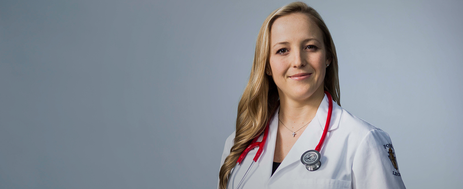 Female student in white coat with pink stethoscope around neck