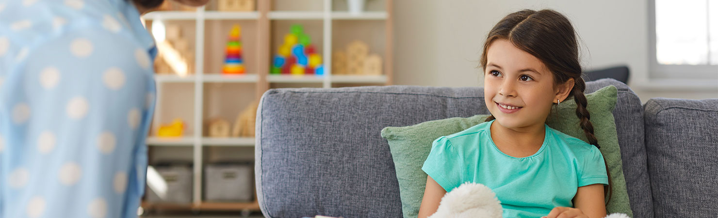 Supportive psychologist with clipboard talking to little girl. Therapist and happy child communicating, analyzing behavior and solving problems during therapy session in cozy modern office