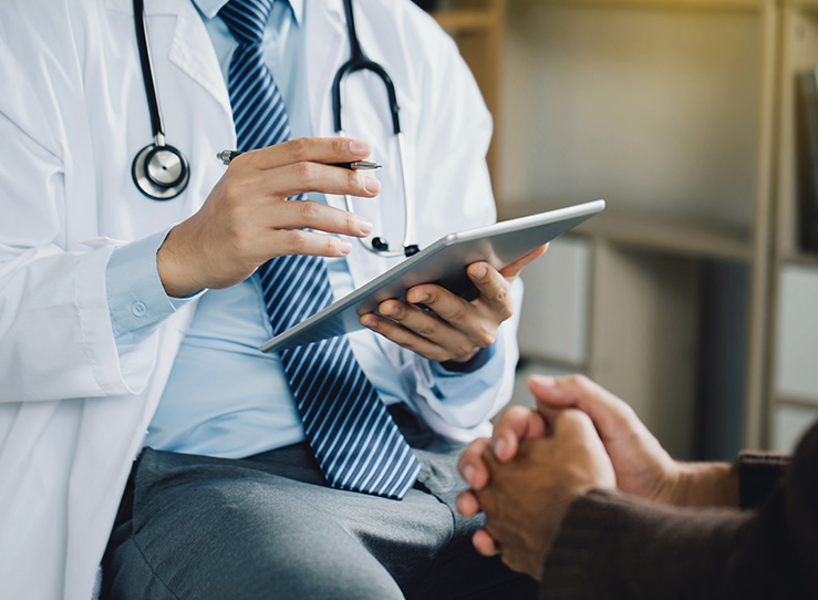 A male doctor with a white coat holding a pen and an iPad.